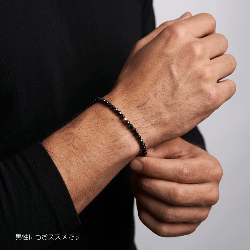 黒いニットの男性がヘマタイトのブレスレットを右腕につけている。